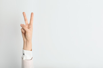 Young woman showing victory gesture on light background. Space for text