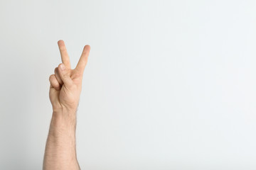 Young man showing victory gesture on light background. Space for text