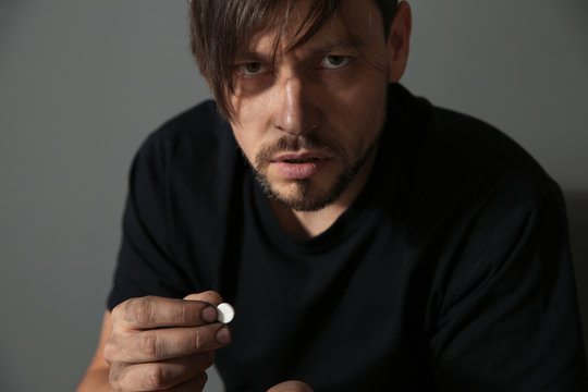Young addicted man with drugs on grey background