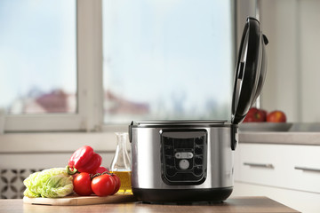 Modern multi cooker and products on table in kitchen. Space for text