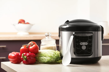 Modern multi cooker and products on table in kitchen. Space for text