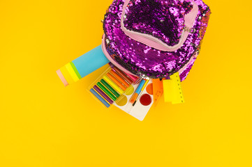 Stationery items from a backpack on a yellow background. Purple girls briefcase with sequins shine.