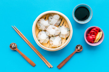 Chinese food set with dim sum, sticks, spices and tea on blue background top view