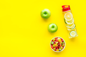 Diet rich in fruits. Slimming diet. Fruit salad near fruit lemon and cucumber water on yellow background top view copy space
