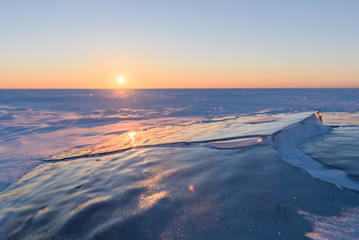 Transparent fragments of ice against the backdrop of the endless snowy landscape during sunset.
