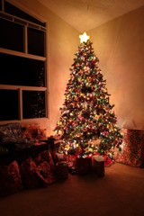A holiday scene in soft warm light inside the family room with a large Christmas tree and several wrapped gifts.