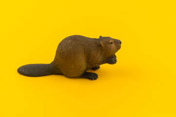 Toy beaver from plastic on a yellow background. © Дарья Колпакова