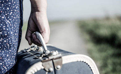 Refugee girl walking with her suitcase out of the road