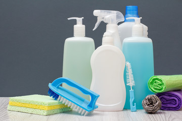 Bottles of dishwashing liquid, brushes and garbage bags on gray background.