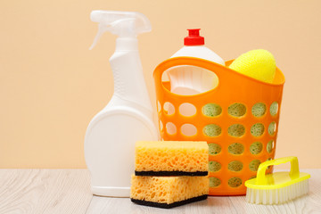 Bottles of dishwashing liquid, basket, brush and sponges on beige background.