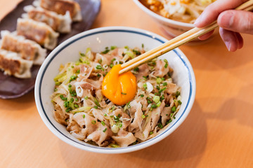 A hand beating yolk on Butadon: Japanese rice bowl dish consisting of pork and onion simmered together and served over rice. Topping with yolk.  