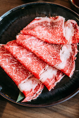 Close up Sukiyaki set including rare slices Wagyu A5 beef with high-marbled texture in black plate.