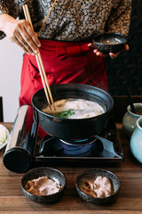 A woman wearing kimono boiling Sukiyaki vegetables set including cabbage, false pak choi, carrot, shiitake, enokitake and tofu.