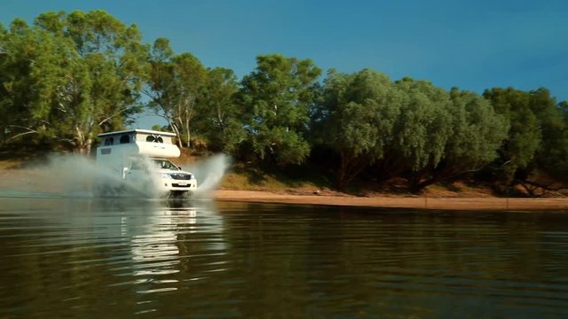 A caravan speeding through water in the outback splashing up big waves