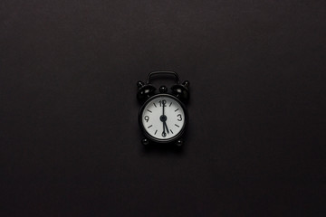 Black alarm clock on a black background. Concept day and night, time management, planning, schedule of day and night, minimalism. Flat lay, top view