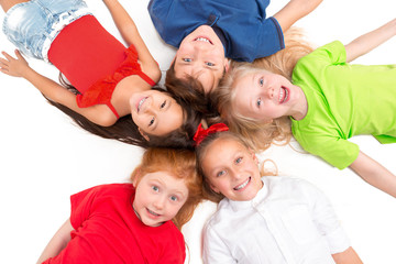 Fototapeta na wymiar Close-up of happy children lying on floor in studio and looking up, isolated on white background, top view. Kids emotions and fashion concept