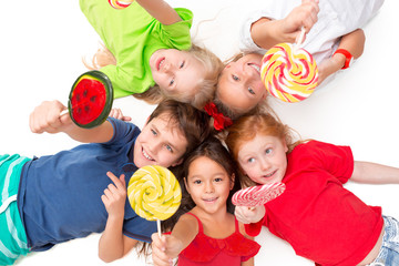 Fototapeta na wymiar Close-up of happy children with candy lying on floor in studio and looking up, isolated on white background, top view. Kids emotions and fashion concept