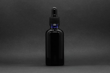 Black bottle with pipette gag on black background with copy space