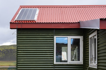 Photo of green small comfort house with red rivets roof and solar panel install on top against peaceful blue sky