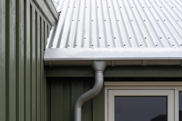 Close up cropped photo of small green house with zinc metallic rain gutter on cornice under rivets roof © brizmaker