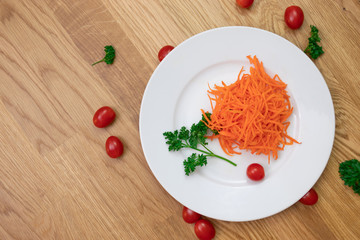 Ground carrot on white plate with parsley and mini tomatoes all around on the wooden table
