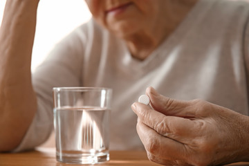 Obraz na płótnie Canvas Elderly woman taking pill at table