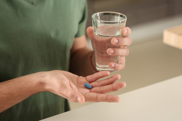 Young man with pill and glass of water indoors, closeup