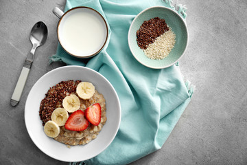 Bowl with tasty oatmeal, sliced banana and strawberry on grey table