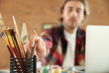 Young designer taking putty knife from holder in office