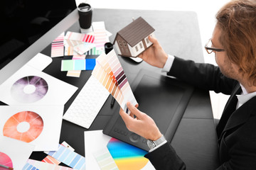 Young designer with color palettes and house model working in office