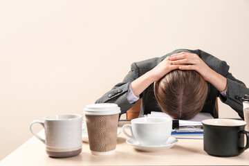 Sleepy businesswoman with a lot of empty cups of coffee sitting at table in office. Concept of addiction