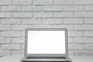 Modern laptop on table against white brick wall