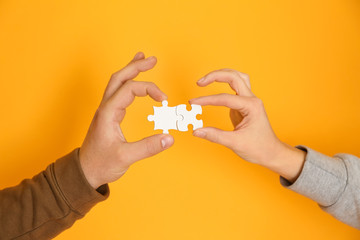Male and female hands with pieces of puzzle on color background