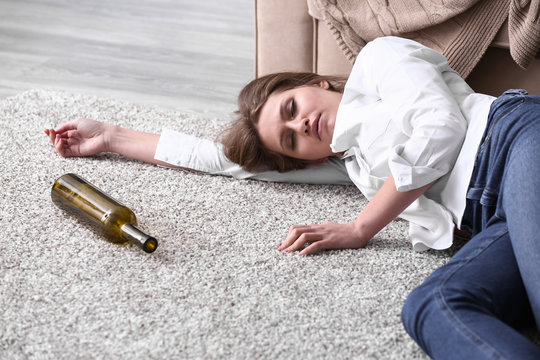Unconscious drunk woman with empty bottle lying on floor