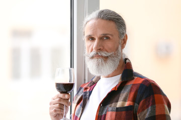 Senior man drinking wine near window at home