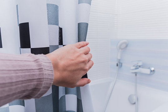 Hand holding shower curtain in white bathroom.