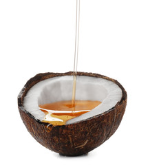 Pouring of oil into half of coconut on white background