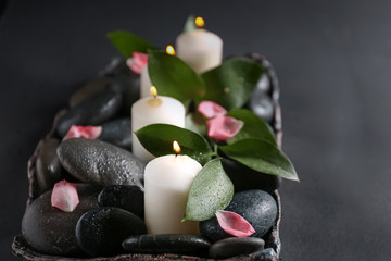 Obraz na płótnie Canvas Tray with beautiful burning candles and spa stones on dark background, closeup