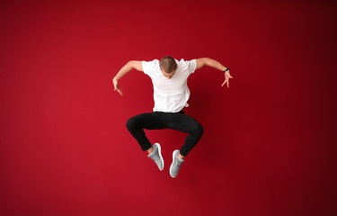 Young male dancer jumping against color background