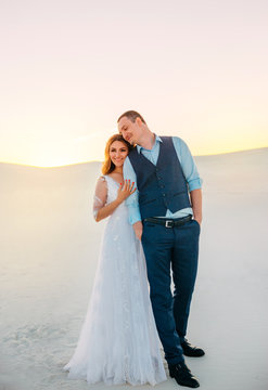 Unusual wedding photo shoot in the desert. Background white sands at sunset. Happy brunette girl with long hair hugging her husband. Fine art photo.