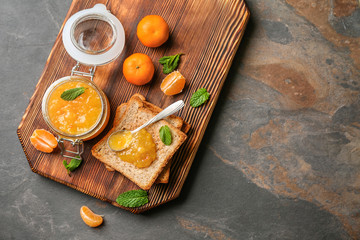 Jar of tasty tangerine jam with toasted bread on wooden board