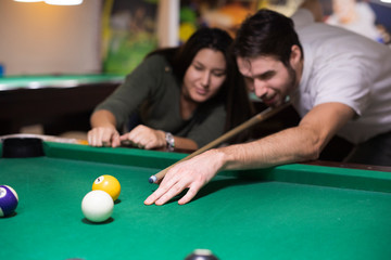 Handsome guy and a beautiful girl are playing billiards