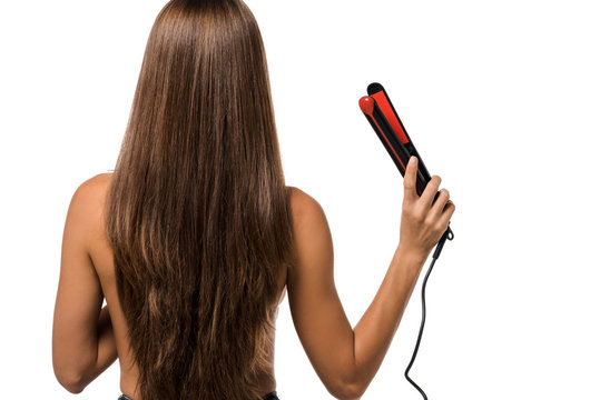 back view of girl with long brown hair holding hair straightener isolated on white
