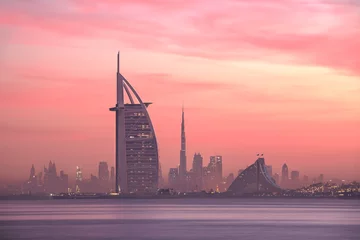 Foto auf Acrylglas Atemberaubende Aussicht auf die Skyline von Dubai vom Jumeirah Beach bis zur Innenstadt, beleuchtet in warmen Pastelltönen des Sonnenaufgangs. Dubai, Vereinigte Arabische Emirate. © Kertu