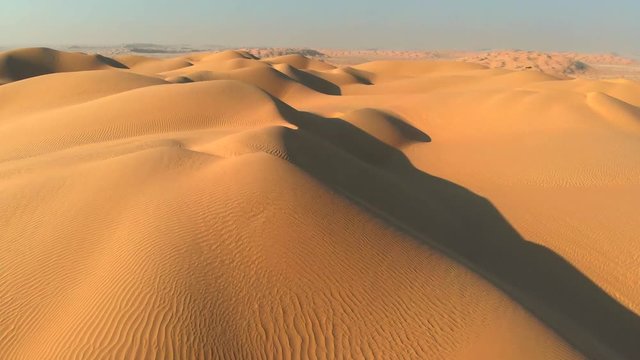 Aerial shot of sand dunes in desert. Flying over endless yellow sand dunes at sunset