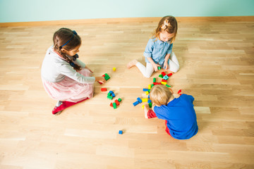Fototapeta premium Three kids playing with wooden blocks in their room