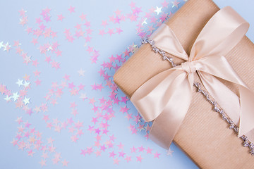 Gift box with beige bow and glitter stars on a pastel blue background.