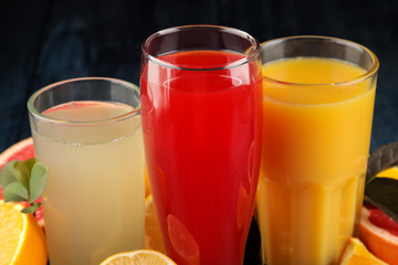Citrus juices. Orange, grapefruit and lemon juice with fresh fruits on a blue wooden table.