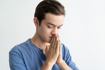 Pensive teenage guy asking for help. Closeup of serious young man in casual putting hands together in pray. Pray concept
