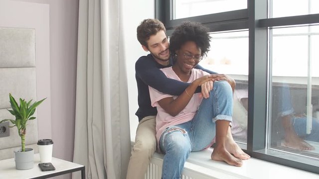 Pretty couple near window. interracial couple. Romantic mixed race couple standing by the window thinking about their future.